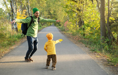 Happy father and son enjoying good weather during fall season. Cheerful dad and child dancing on the empty road in autumn park. Parenting and childhood.
