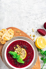 Red beetroot cream soup with lemon and seeds in a white bowl on a gray concrete background top view. Free space for text. Beetroot and vegetable puree soup. Vegetarian and diet food. Copy space.