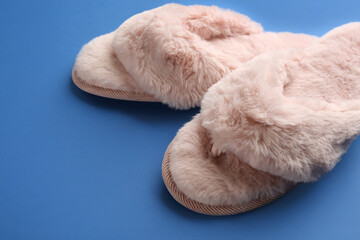 Fototapeta na wymiar Pair of stylish soft slippers on blue background, closeup