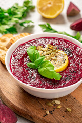 Red beetroot cream soup with lemon and seeds in a white bowl on a gray concrete background. Beetroot and vegetable puree soup. Vegetarian and diet food.