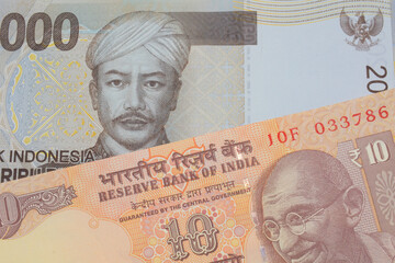 A macro image of a orange ten rupee bill from India paired up with a grey two thousand Indonesian rupiah bank note.  Shot close up in macro.