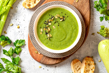 Green vegetable cream soup in a white bowl on a gray concrete background top view. Vegan soup puree of green vegetables. Vegetarian and diet food.