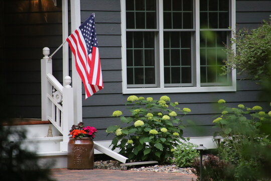 A stereotypical American home's front entrance, with the American flag hanging by the front door.