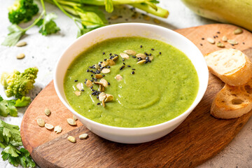 Green vegetable cream soup in a white bowl on a gray concrete background. Vegan soup puree of green vegetables. Vegetarian and diet food.