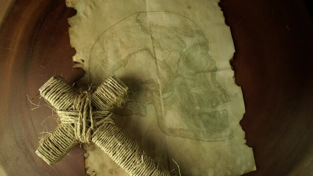 Ancient parchment with human skull drawing and Christian Crucifix cross on wooden tree trunk table. Religion Jesus Christ cross made of forest twigs and rope. Cemetery and resurrection concept. 