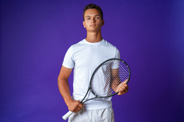 Caucasian young man tennis player posing with tennis racket against purple background