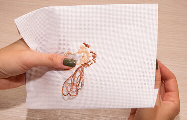 Women's hands hold an embroidery canvas and embroider with a cross on a wooden background