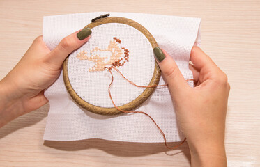 Women's hands hold a white canvas in a hoop with a needle and embroider with a cross