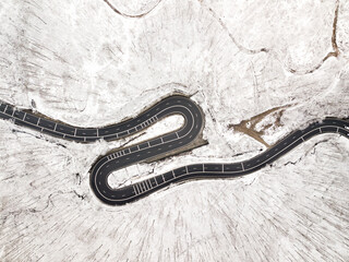 Curvy windy road in snow covered forest, top down aerial view.