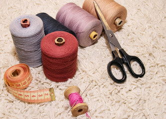 Large five spools of thread, a meter, a spool of pink thread with a needle and scissors lie on a...