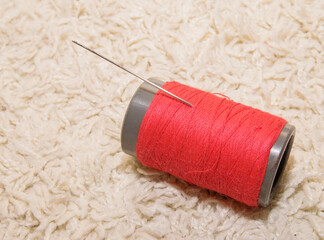 A spool of red thread with a needle lies on a white background