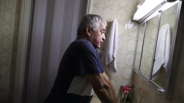 Troubled senior man looking at bathroom mirror suffering mental illness