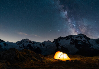 A tent in the mountains under the night sky and milky way.