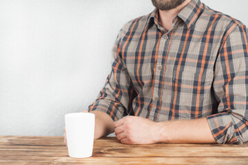 A young man in a shirt holds a cup in his hand. Office worker. Sitting at a wooden table