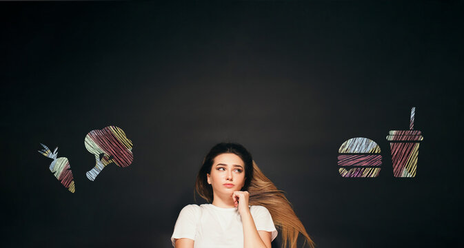 Hesitating woman making decision between with chalk drawn food icons vegetables and fast food, concept healthy lifestyle and dieting