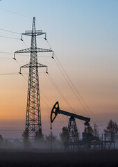 Silhouettes of oil pump and high-voltage transmission line support in morning fog at sunrise