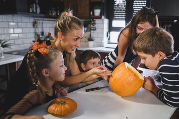 Fototapeta premium Mother carving Halloween pumpkin with children, making jack-o-lanterns