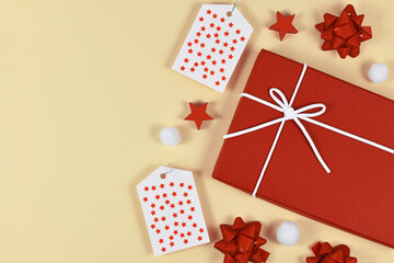 Christmas present gift wrapping concept with red gift box, ribbons, gift labels and white snow balls on yellow background with empy copy space