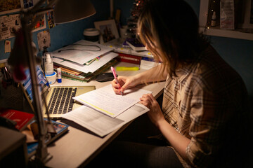 A girl is preparing for exams, writing at a table in the dark