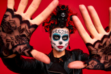 Scary young creepy lady calavera. wears artistic make-up for the feast of all the dead.Wears black leather jacket and lace gloves, dressed as skeleton isolated in red.