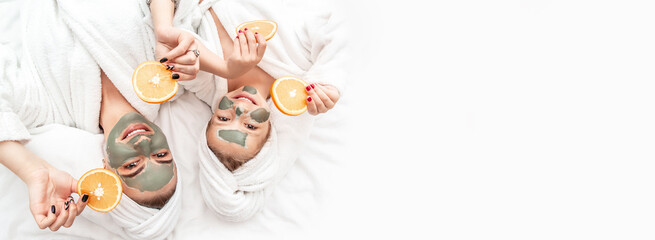 Happy family mother and child daughter make face skin mask with towel on head, holding slices of oranges on white background, Facial skin care, cosmetology Long banner format