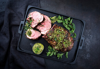 Traditional English barbecue lamb roast sliced with mint leaf and sauce offered as top view in a design cast-iron tray with copy space right