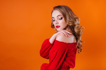 Fototapeta premium A young beautiful girl shows emotions and smiles in the Studio on an orange background. Girls for advertising