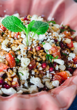 Barley salad with pomegranate, feta and mint on a pink ceramic and denin napkin
