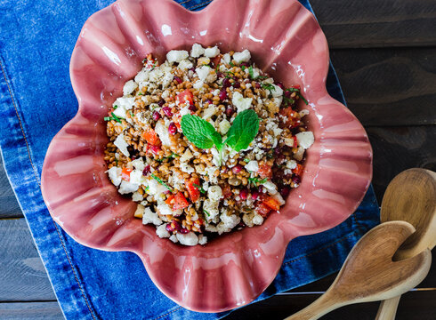 Barley salad with pomegranate, feta and mint on a pink ceramic and denin napkin