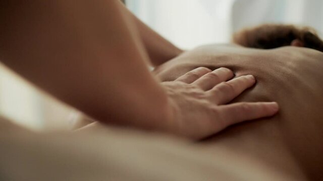 Closeup professional masseur touching and stroking female client back massaging relaxing muscles