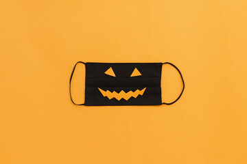 Halloween 2020 safe celebration. Evil face mask flat lay on orange background with copy space