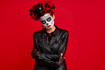 Sugar skull pretty girl with halloween makeup standing on bright red background. Wonderful female zombie with flowers in hair celebrating day of the dead.