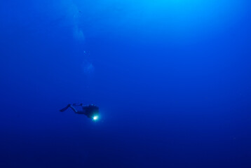 A scuba diver in the deep blue looking small against the might of the ocean