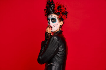 Dead gir with sugar skull makeup with a wreath of flowers on her head and skull, wearth black gloves opene her mouth in shock isolated on red background. concept of Halloween or La Calavera Catrina