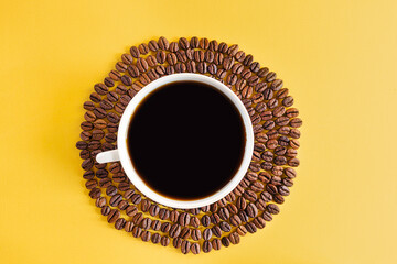 White cup and coffee beans on a yellow background. Creative concept for coffee shops. Top view, copy space, minimalism, conceptual flat lay.