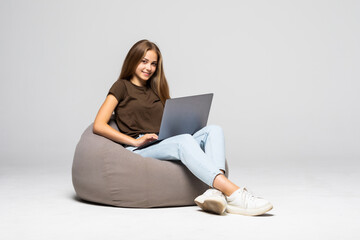 Happy young woman sitting on the floor using laptop on gray background