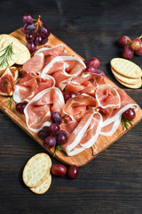 Traditional Italian antipasti prosciutto crudo with grapes and crackers on a wooden plate. Spanish jamon. Food for aperitif and dinner lunch in the restaurant. top view