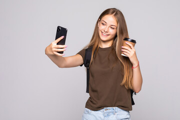 Fototapeta premium Portrait of a smiling attractive woman in suit taking a selfie while holding take away coffee cup over white background