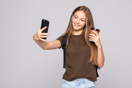 Portrait of a smiling attractive woman in suit taking a selfie while holding take away coffee cup over white background