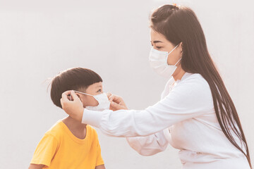 Fototapeta premium Mom is wearing a medical mask for her child. Little asian boy and mom in medical mask. Asian family protection virus concept.