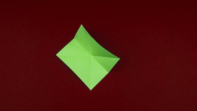 Creative paper Christmas tree. Origami. Stop motion. Hand made. Christmas tree sequentially folded from four sheets of paper on red background. 4K video.