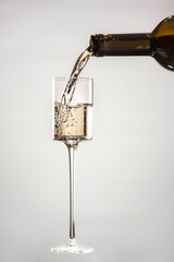 White wine pouring from bottle into glass isolated on gray background
