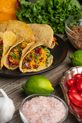 Close-up view of plate with tasty mexican tacos on rustic wooden table with ingredients for cooking background. Concept of traditional meal. Backstage of preparing food. Mexican cuisine.