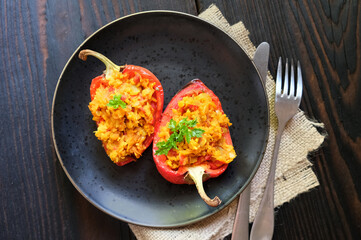 Homemade baked stuffed peppers filled with red lentils with vegetables on a dark plate, wooden background