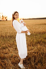 Wonderful mother with beautiful little daughter walking at the field, elegant mom hold cute newborn baby girl in arms, happy family moments, parenting and maternity concept