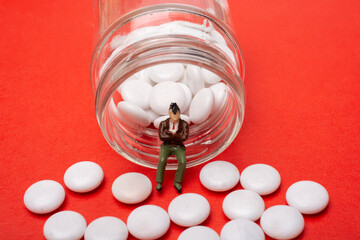 Pills spilling out from  container where  man figurine sitting.   healthcare.
