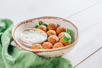 Bowl of falafel with tzatziki sauce on a white wooden table.