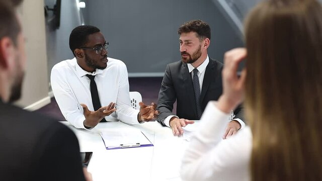Businessman in suit talking to business people colleagues or partners sitting at conference table, male leader discussing work at team meeting or group negotiations having conversation with clients