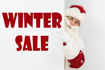 Santa Claus points his fingers at the board with the text - WINTER SALE