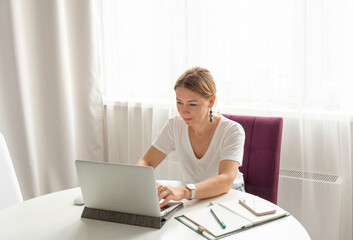 middle-aged woman works on a laptop at home in a light interior at a remote job